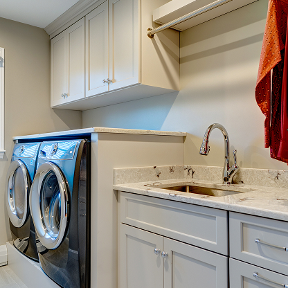 Modern laundry room with white shaker cabinets, marble countertops, stainless steel washer dryer and utility sink