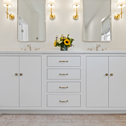 Double vanity with brass sconces, white cabinets, and central storage drawers