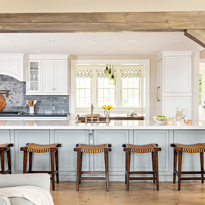 Modern farmhouse kitchen with white cabinets, blue backsplash, wooden beam, and rattan counter stools at marble island
