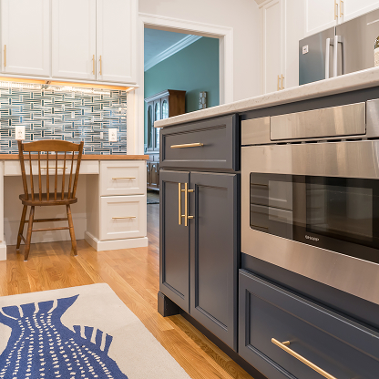 Modern kitchen design with navy blue base cabinets, glass tile backsplash, and built-in desk nook