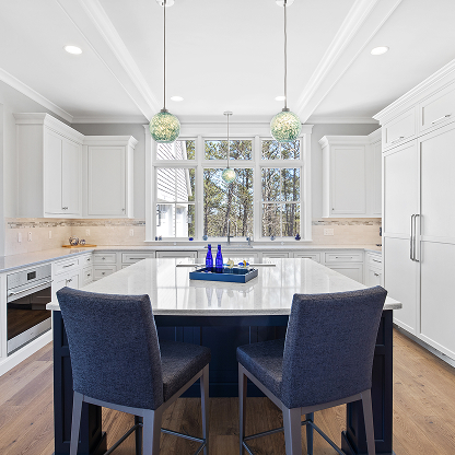 White kitchen with navy island, glass pendant lights, and large windows overlooking nature
