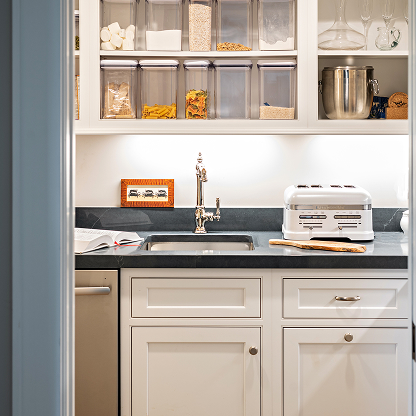 White butler's pantry with glass storage containers, black countertops and built-in appliances