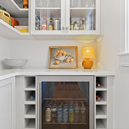 White pantry with built-in beverage fridge, glass cabinets and orange accent lamp