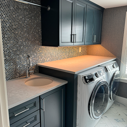 Modern laundry room with navy cabinets, penny tile backsplash and quartz countertops