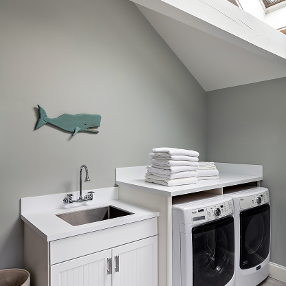 Coastal laundry room with whale decor, white cabinets and stacked washer dryer