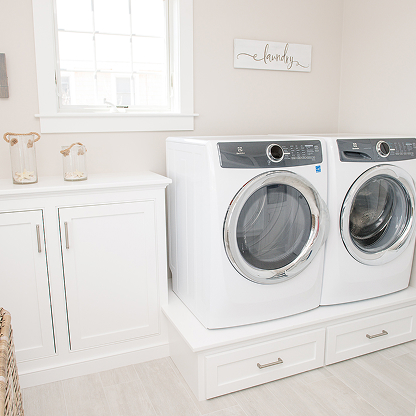 White laundry room with pedestal washer dryer, built-in storage and farmhouse decor