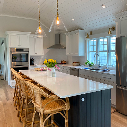 Coastal kitchen with navy island, rattan bar stools and glass pendant lights