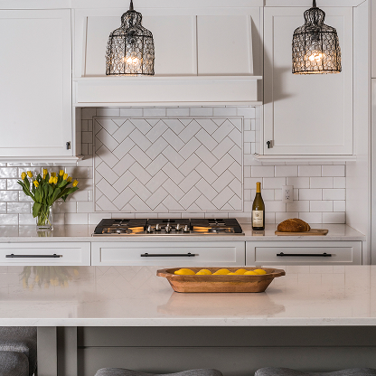 White kitchen with herringbone backsplash, wire cage pendants and quartz countertops