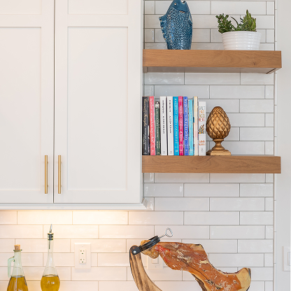 Modern kitchen detail with floating wood shelves, white subway tile backsplash, brass cabinet pulls, under-cabinet lighting, and decorative accessories