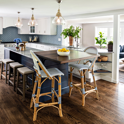 Modern kitchen with blue herringbone backsplash, French bistro barstools, navy island with wood extension, glass pendant lights, and indoor plants