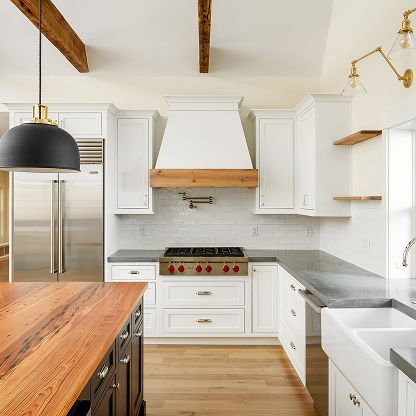 Farmhouse kitchen with custom wood hood, white cabinets, butcher block island and brass fixtures - modern rustic design
