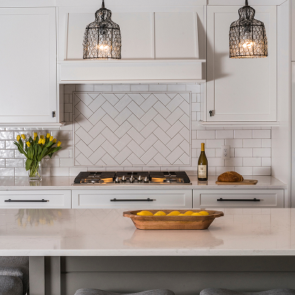 White kitchen with herringbone tile backsplash, pendant lighting, and wooden fruit bowl on counter