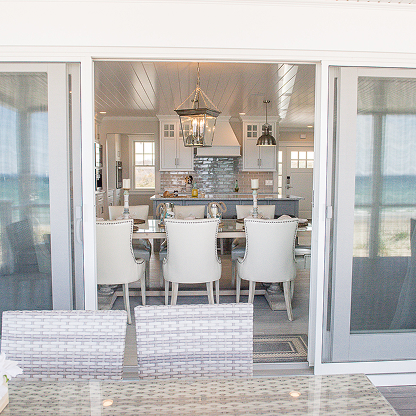Coastal kitchen with sliding glass doors, white upholstered chairs, and lantern pendant lighting
