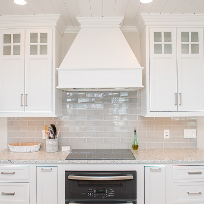 White shaker kitchen cabinets with custom range hood and iridescent glass tile backsplash
