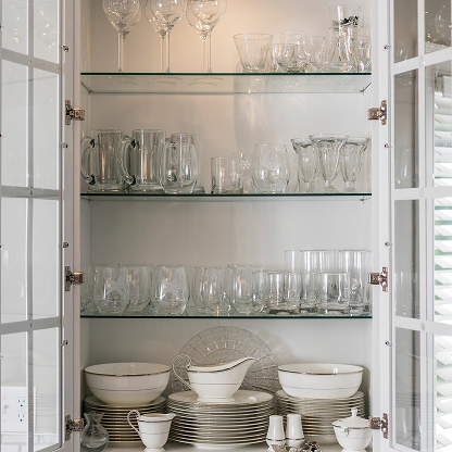 Glass-front cabinet with crystal stemware, glassware, and white dinnerware on glass shelves