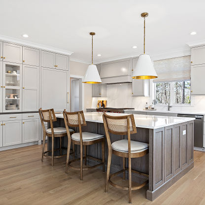 Modern kitchen with white and gold pendant lights, cane back bar stools, and gray island