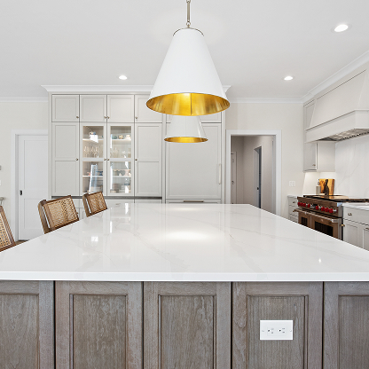 Kitchen island with white quartz countertop, gold-lined pendant lights, and gray base cabinets