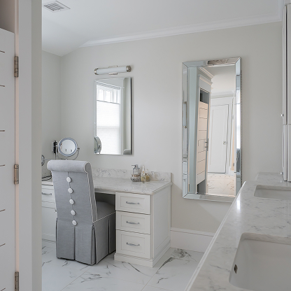 Elegant makeup vanity with upholstered chair, marble countertop, and framed mirrors