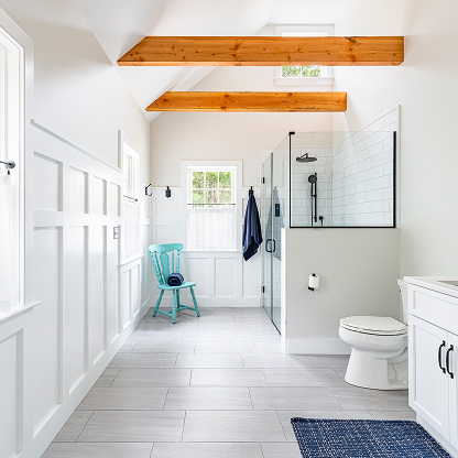 Farmhouse bathroom with exposed wood beams, glass shower, and turquoise accent chair