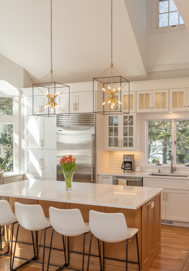 A bright, modern kitchen with white cabinets, stainless steel appliances, a central island, and large windows letting in natural light.